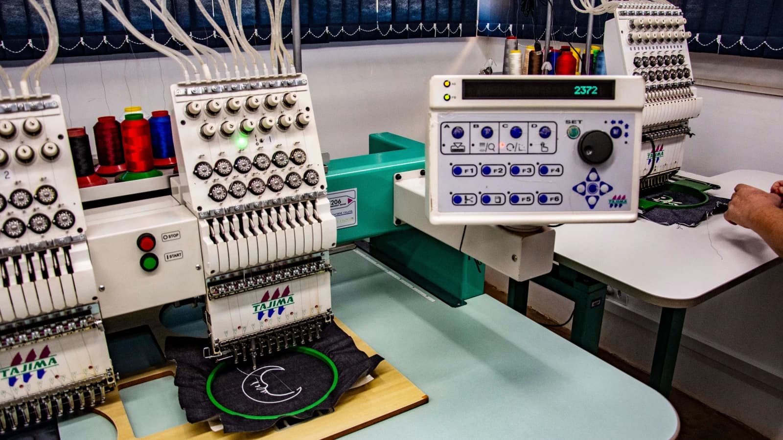 Multi-head embroidery machines stitching a crescent design into dark fabric
