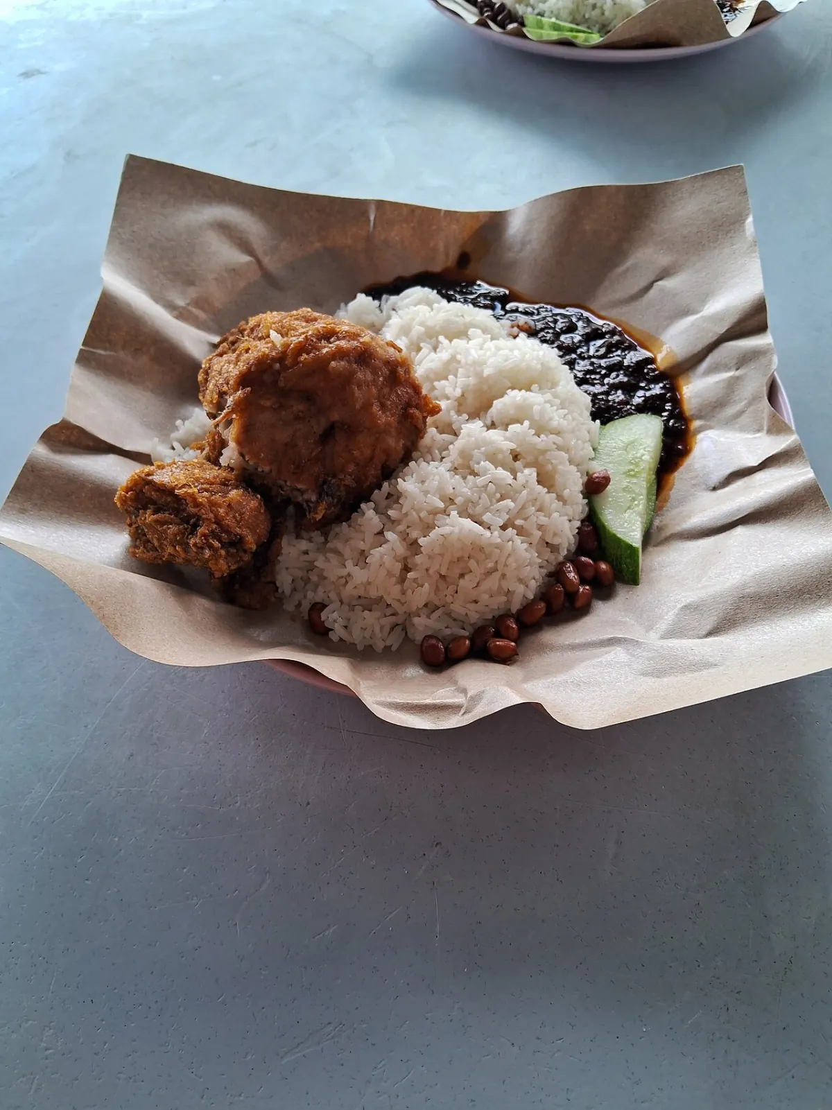Nasi lemak with fried chicken, coconut rice, dark sambal, cucumber and peanuts on brown paper