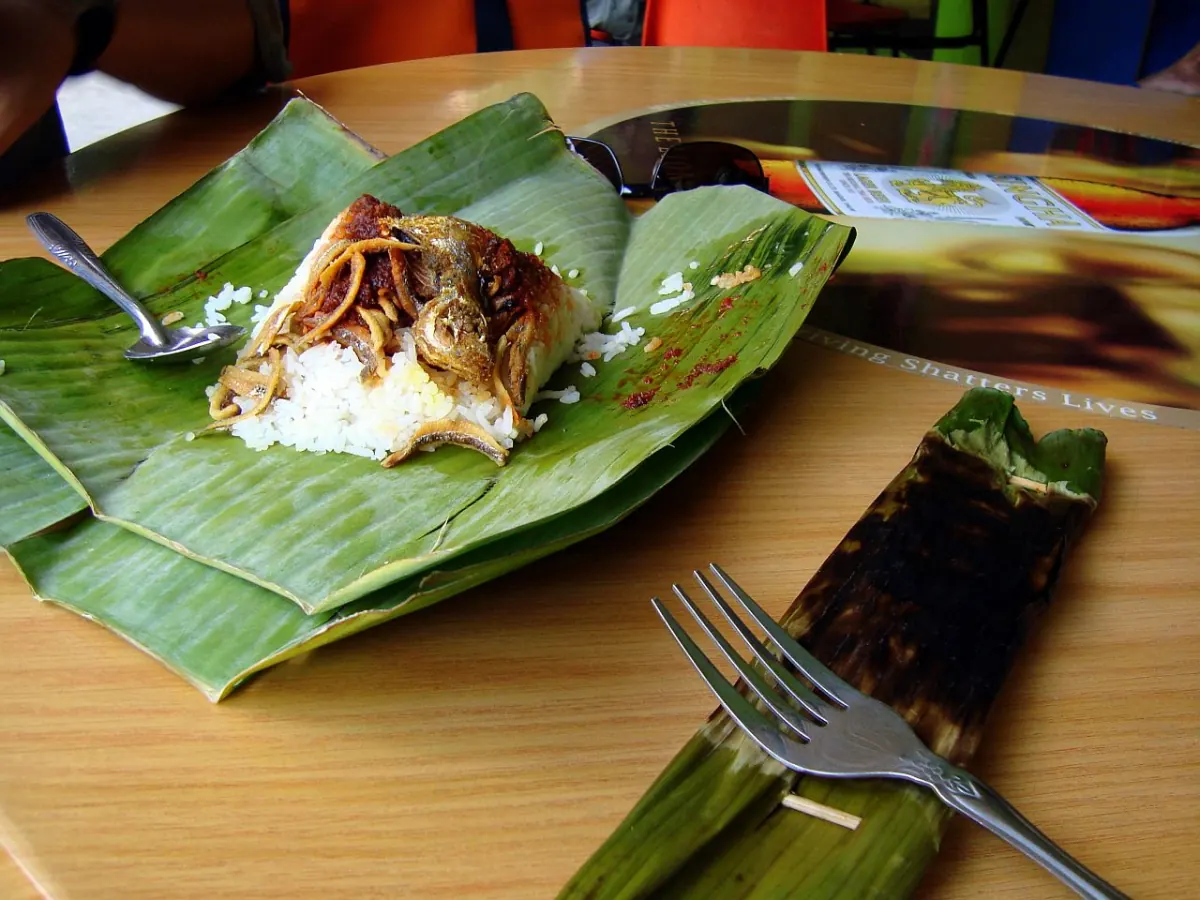 A banana-leaf nasi lemak parcel opened beside a wrapped otak-otak